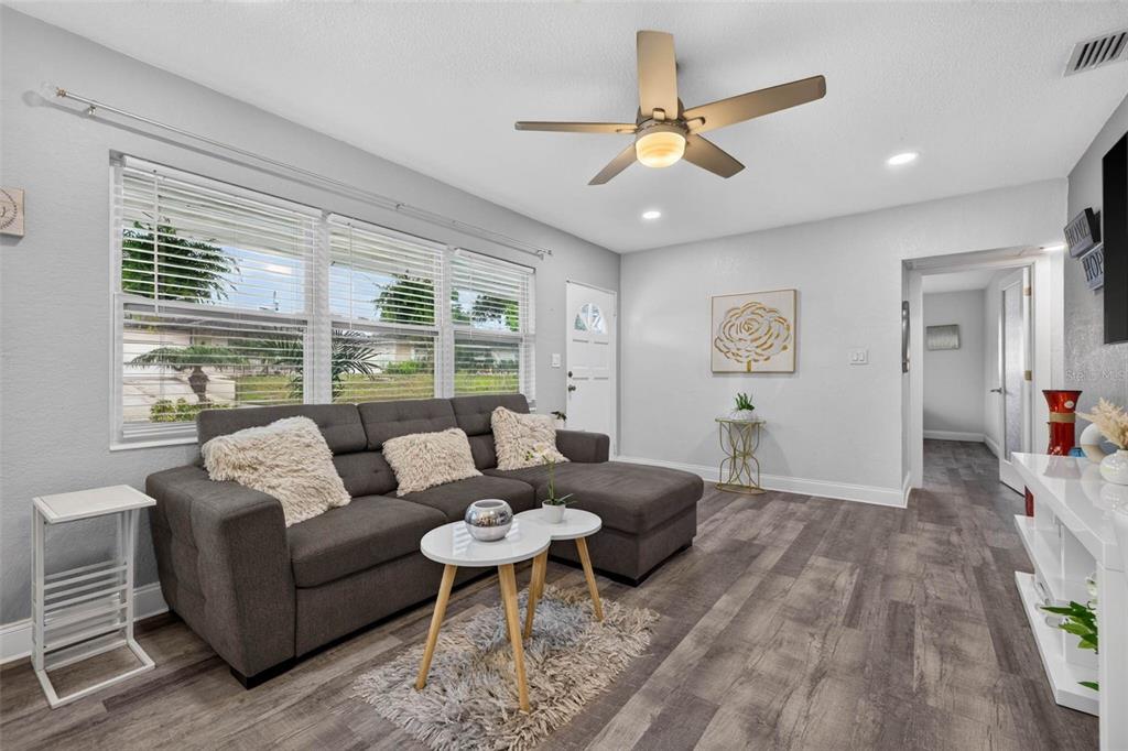 A living room features a gray sectional sofa, wood-look flooring, and a ceiling fan — 3164 52ND WAY N, ST PETERSBURG, FL