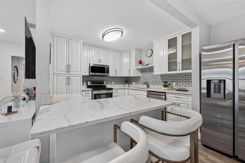 A modern kitchen features white cabinetry, marble countertops, a breakfast bar, and stainless steel appliances — 3164 52ND WAY N, ST PETERSBURG, FL