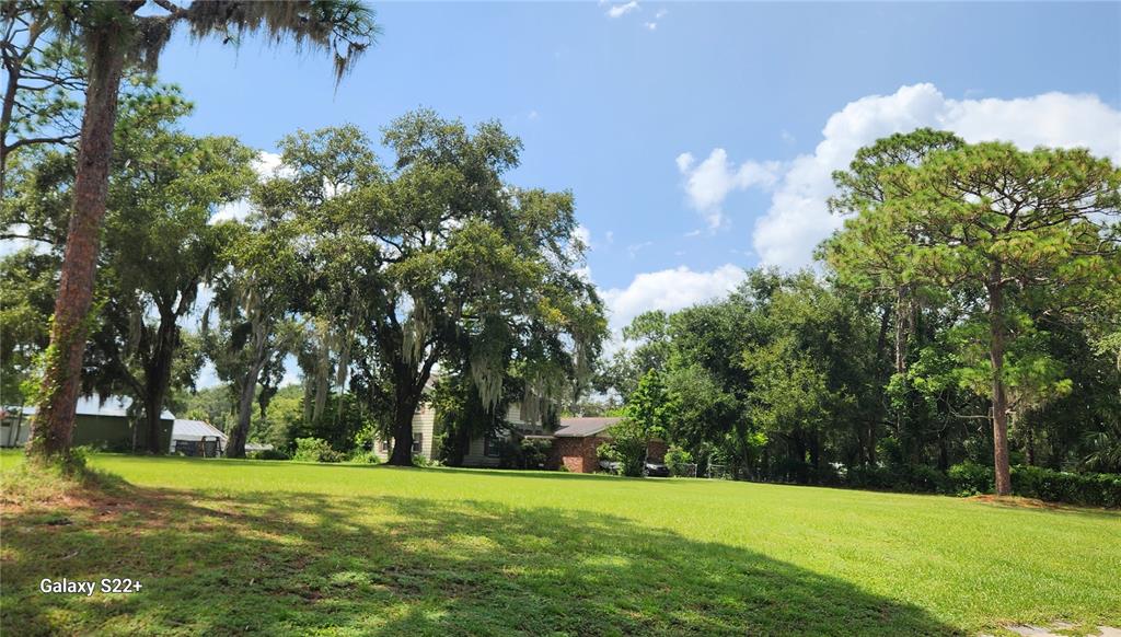 A large, grassy lawn leads to a house partially obscured by mature trees and foliage — 1048 USTLER ROAD, APOPKA, FL