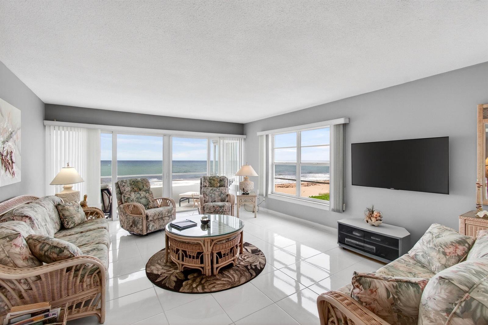 A living room with wicker furniture, tile floors, and large windows overlooking the ocean — 2701 S Ocean Boulevard # 21, Highland Beach FL 33487, HIGHLAND BEACH, FL