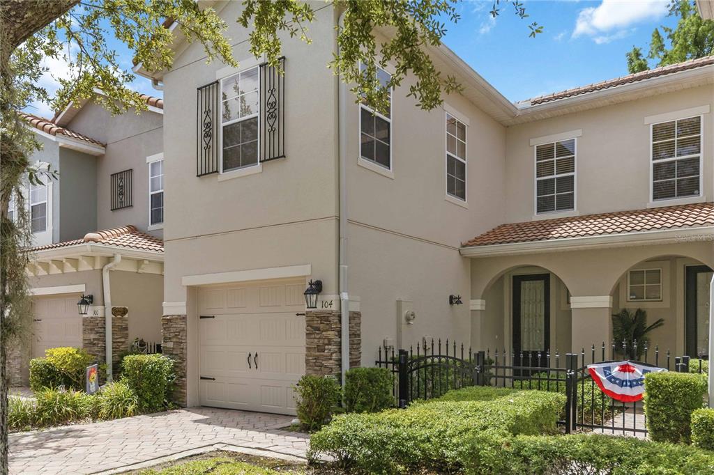 A two-story townhouse exterior with a tan stucco facade, stone accents, and a paved driveway — 104 CANTERBURY BELL DRIVE, OVIEDO, FL