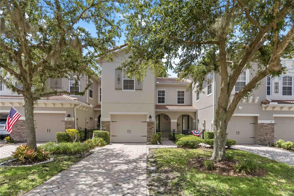A row of three two-story townhomes with beige stucco facades, stone accents, and paved driveways — 104 CANTERBURY BELL DRIVE, OVIEDO, FL