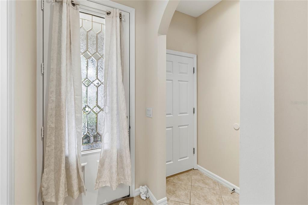 An entryway features a white door with a decorative glass insert, curtains, and tiled flooring — 104 CANTERBURY BELL DRIVE, OVIEDO, FL