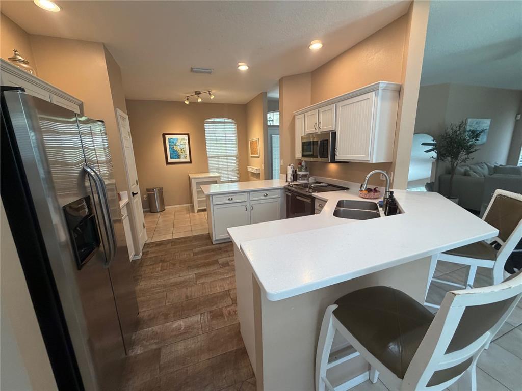 A kitchen features white cabinets, stainless steel appliances, a breakfast bar, and wood-look tile flooring — 217 36TH STREET NE, BRADENTON, FL