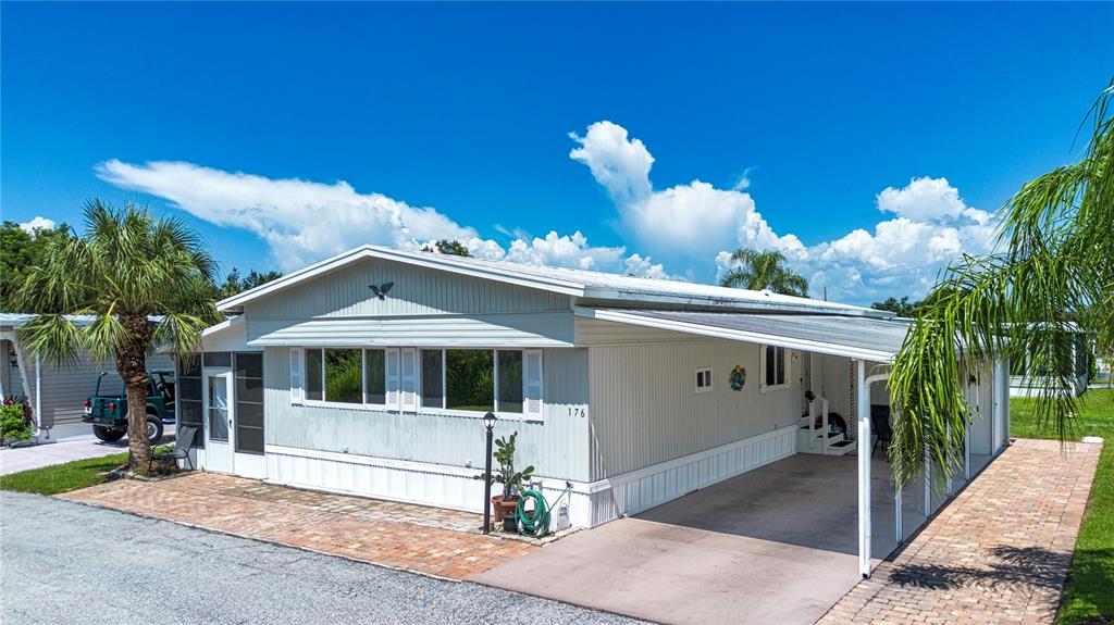 A light-colored mobile home features a brick driveway, a carport, and a palm tree — 420 49TH STREET E UNIT 176, PALMETTO, FL