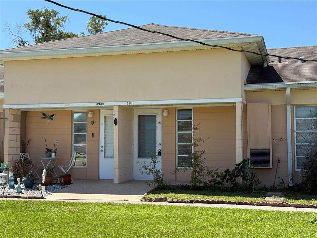 A duplex exterior features beige siding, two white front doors, and a shared concrete porch — 3911 CLUB CIRCLE, LAKE WALES, FL