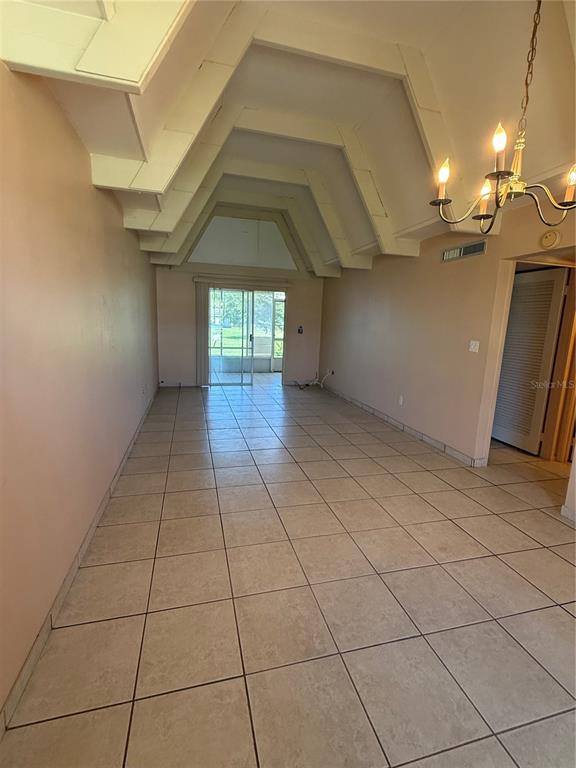 An empty living room features vaulted ceilings, tile flooring, and a sliding glass door — 3911 CLUB CIRCLE, LAKE WALES, FL