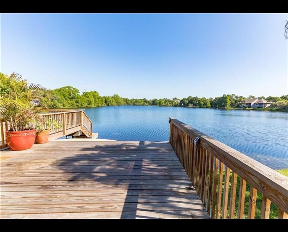A wooden deck overlooks a calm lake surrounded by trees under a clear blue sky — 2644 SABAL SPRINGS DRIVE UNIT 3, CLEARWATER, FL
