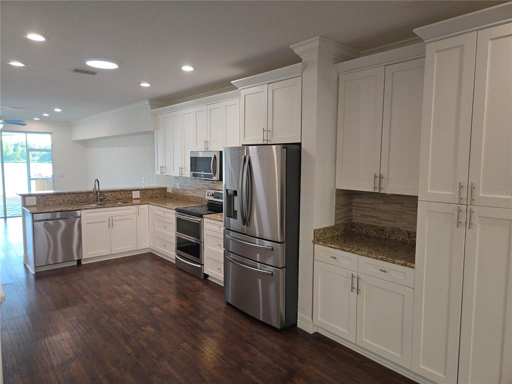 A kitchen features white cabinetry, stainless steel appliances, granite countertops, and dark wood flooring — 2644 SABAL SPRINGS DRIVE UNIT 3, CLEARWATER, FL