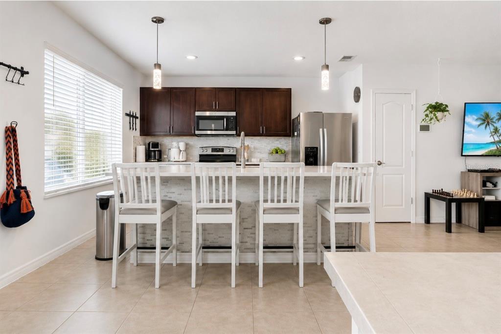 A kitchen features dark wood cabinets, stainless steel appliances, a breakfast bar, and white stools — 1779 RED CANYON DRIVE, KISSIMMEE, FL