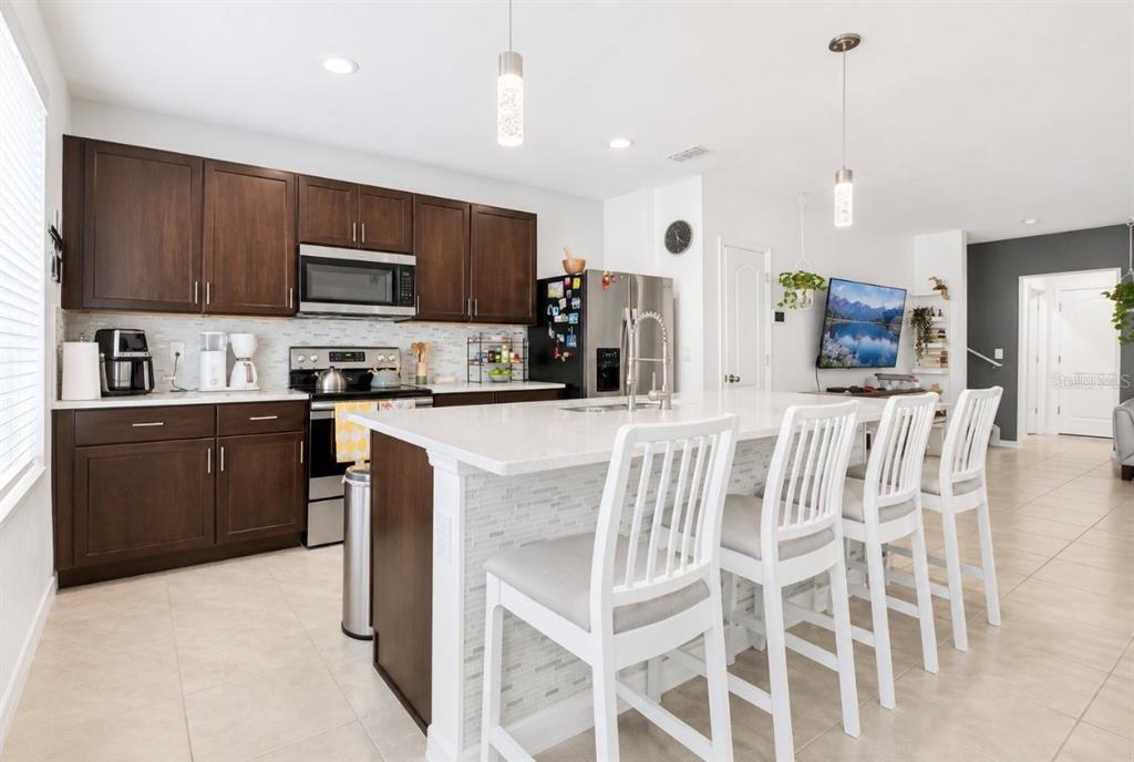 A modern kitchen features dark wood cabinets, a white quartz island, and four white chairs — 1779 RED CANYON DRIVE, KISSIMMEE, FL