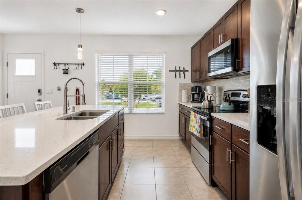 A kitchen features dark wood cabinets, stainless steel appliances, a quartz island, and tile flooring — 1779 RED CANYON DRIVE, KISSIMMEE, FL