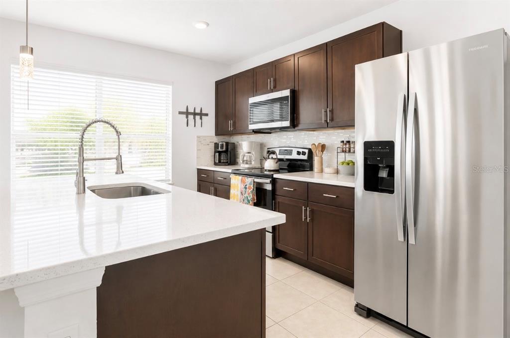 A kitchen features dark wood cabinets, stainless steel appliances, and a white quartz island countertop — 1779 RED CANYON DRIVE, KISSIMMEE, FL