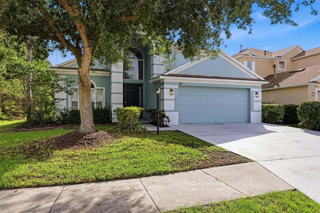 A two-story light blue house with a two-car garage and a large front tree — 6417 BLUE GROSBEAK CIRCLE, BRADENTON, FL