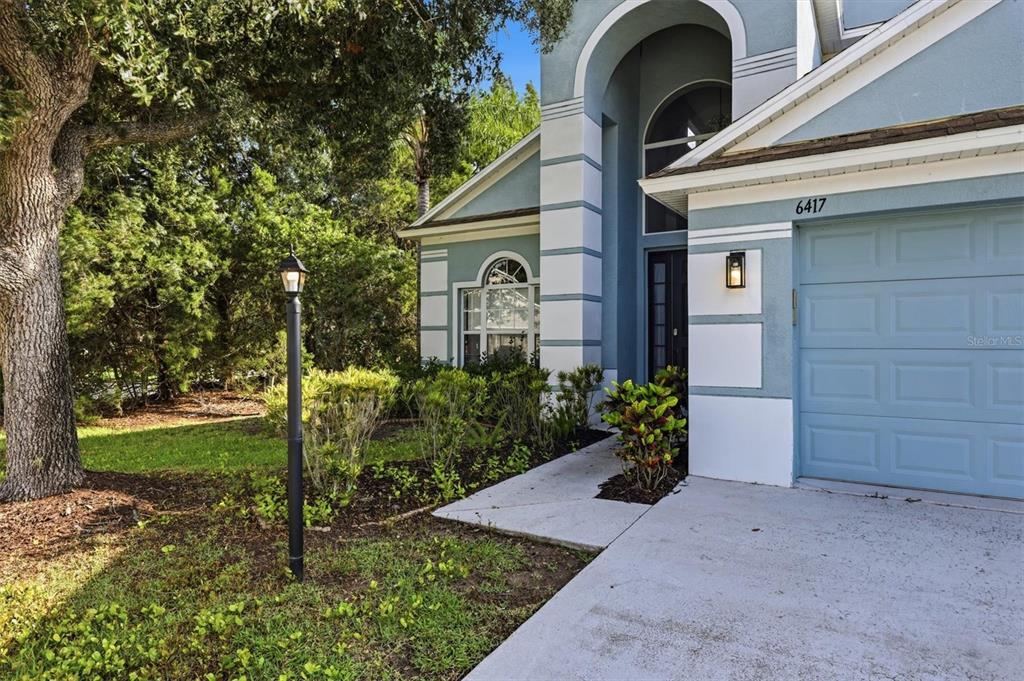 The exterior of a blue house features a garage, a front entryway, and a lamp post — 6417 BLUE GROSBEAK CIRCLE, BRADENTON, FL