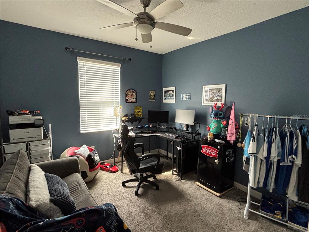 A bedroom features a desk, gaming chair, sofa, clothing rack, and blue walls — 4697 FAIRY TALE CIRCLE, KISSIMMEE, FL