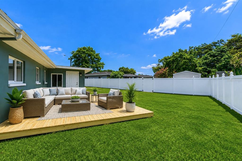 A wooden deck with patio furniture sits in a backyard next to a green house — 1800 DRUID ROAD E, CLEARWATER, FL