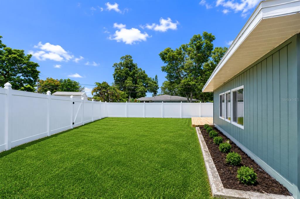 A backyard features a green lawn, a white vinyl fence, and a teal house exterior — 1800 DRUID ROAD E, CLEARWATER, FL