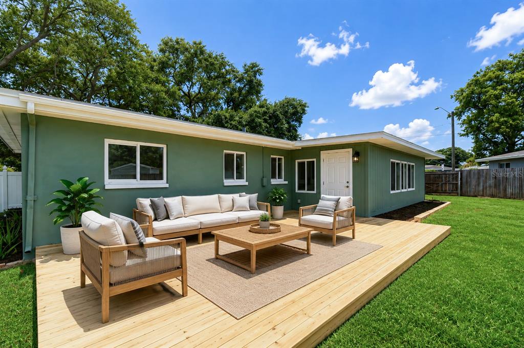 A green house exterior features a wooden deck with outdoor furniture and a grassy yard — 1800 DRUID ROAD E, CLEARWATER, FL
