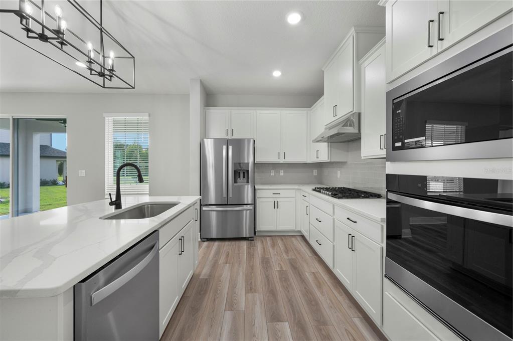 A modern kitchen features white cabinets, stainless steel appliances, a center island, and wood-look flooring — 7883 SOMERSWORTH DRIVE, KISSIMMEE, FL