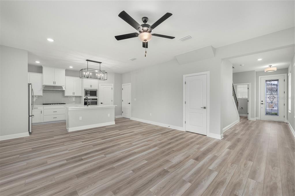 An open-concept kitchen and living area with white cabinets, light wood floors, and a ceiling fan — 7883 SOMERSWORTH DRIVE, KISSIMMEE, FL