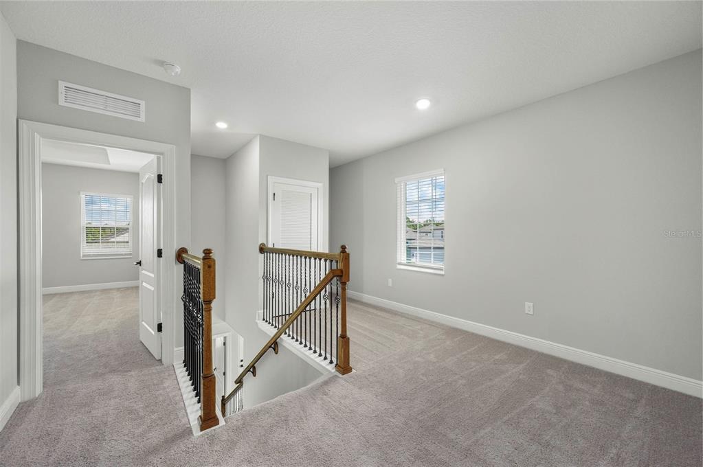 A carpeted landing features a wooden staircase with iron railings and two white doors — 7883 SOMERSWORTH DRIVE, KISSIMMEE, FL