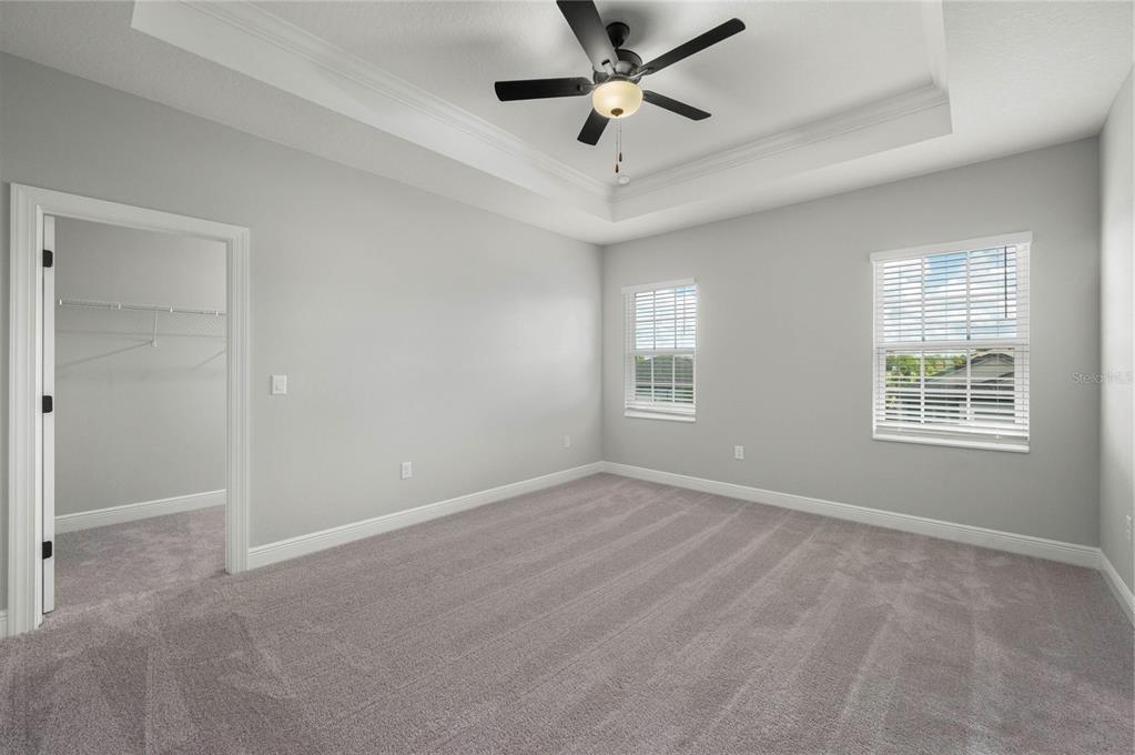 An empty bedroom features gray carpet, light gray walls, a tray ceiling, and two windows — 7883 SOMERSWORTH DRIVE, KISSIMMEE, FL