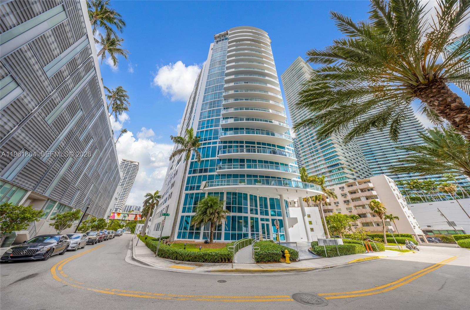 A low-angle exterior view of a modern glass high-rise condominium building on a city street — 480 NE 30th St # 1402, Miami FL 33137, MIAMI, FL