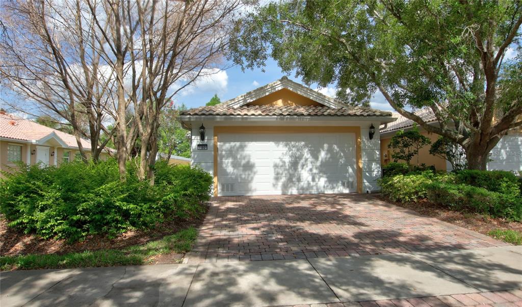A single-story house exterior features a white garage door, a tiled roof, and a brick driveway — 11801 FAN TAIL LANE, ORLANDO, FL