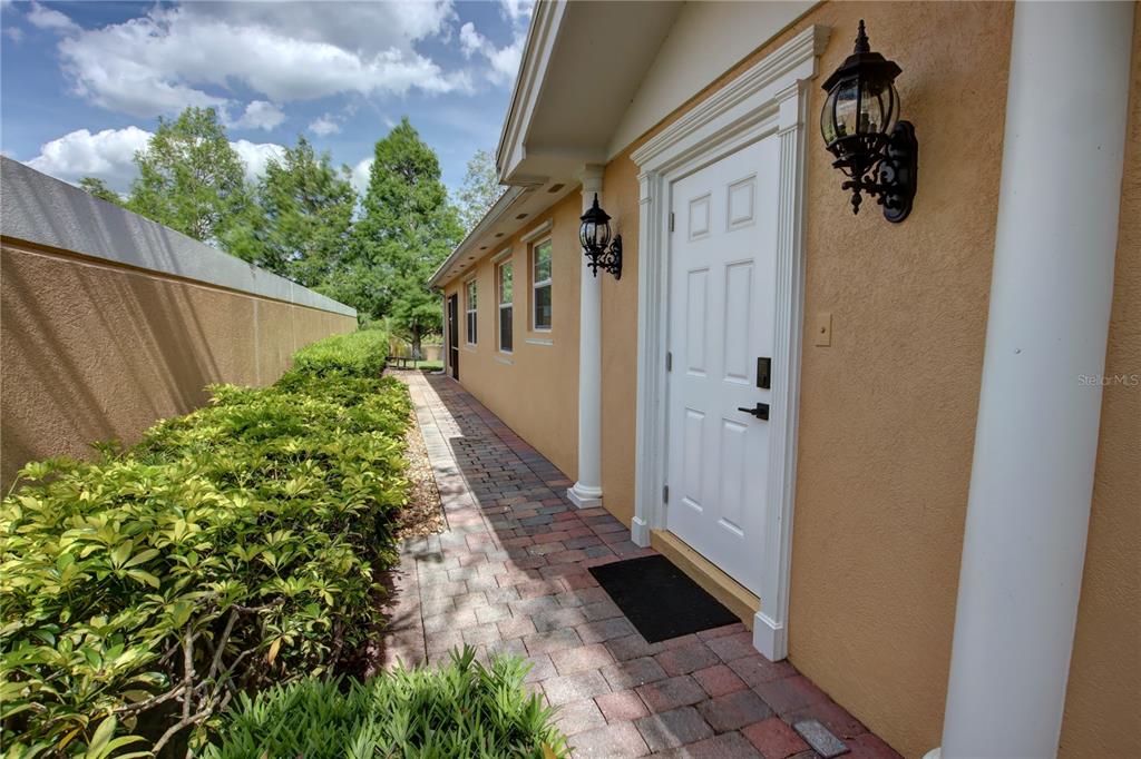 A paved walkway leads along the side of a house with a white door — 11801 FAN TAIL LANE, ORLANDO, FL
