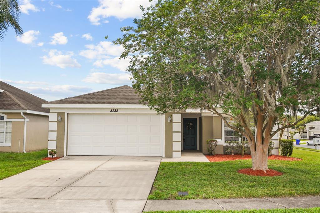 A single-story house with a white garage door, tan stucco exterior, and a large tree — 3222 WHOOPING CRANE RUN, KISSIMMEE, FL