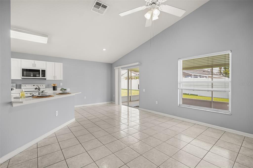 A kitchen with white cabinets and a breakfast bar opens to a tiled living area — 3222 WHOOPING CRANE RUN, KISSIMMEE, FL