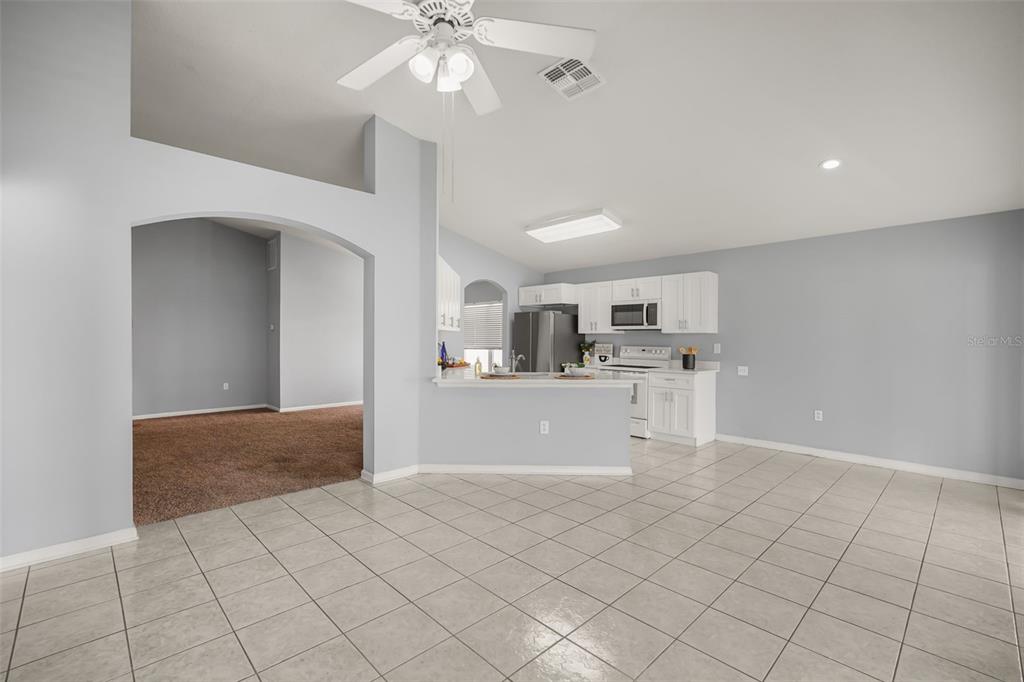 A kitchen with white cabinets and tile flooring opens to a carpeted living area — 3222 WHOOPING CRANE RUN, KISSIMMEE, FL