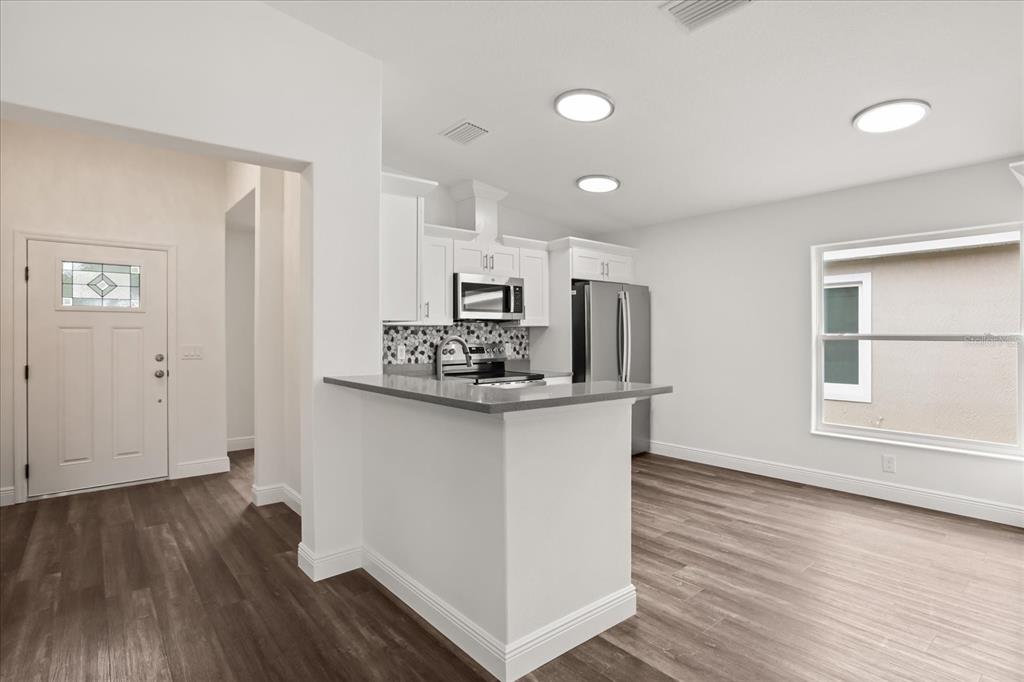 A kitchen with white cabinets, gray countertops, and stainless steel appliances opens to a dining area — 706 BEECHER STREET, LEESBURG, FL