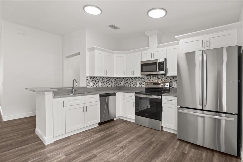 A kitchen features white cabinets, stainless steel appliances, gray countertops, and wood-look flooring — 706 BEECHER STREET, LEESBURG, FL
