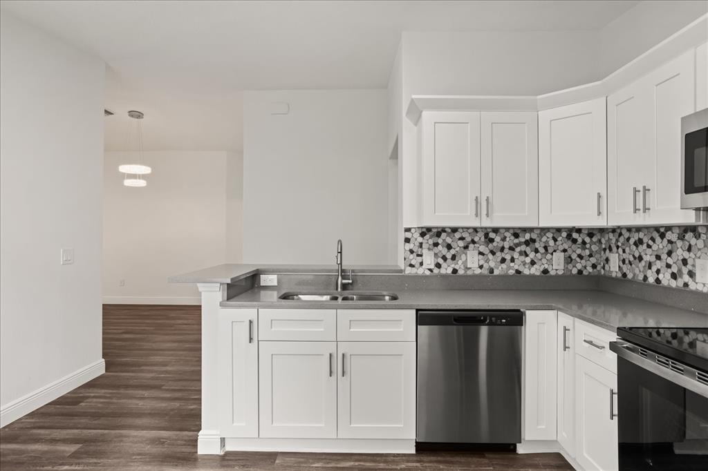A kitchen features white cabinets, gray countertops, a mosaic backsplash, and stainless steel appliances — 706 BEECHER STREET, LEESBURG, FL