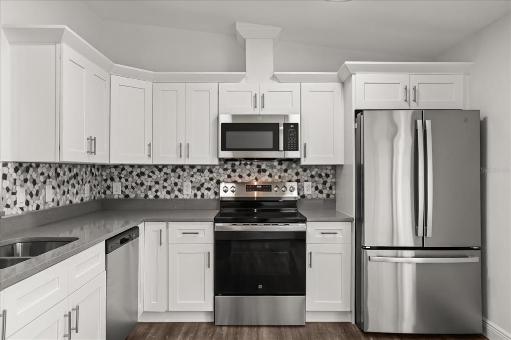 A kitchen features white cabinets, stainless steel appliances, a gray countertop, and a patterned backsplash — 706 BEECHER STREET, LEESBURG, FL
