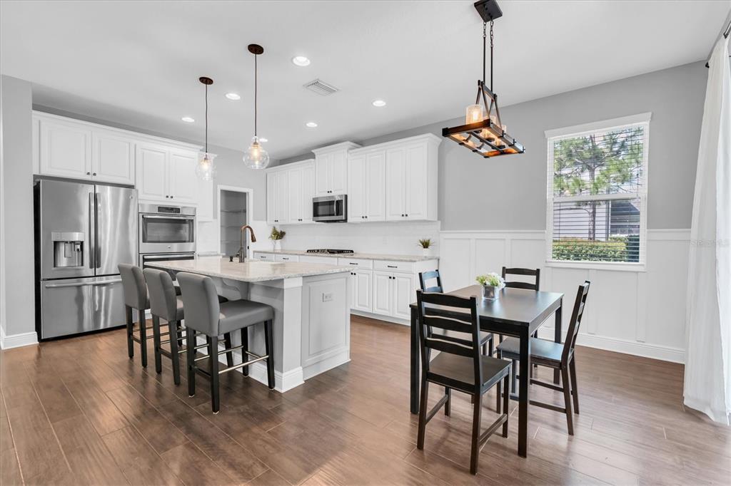 A kitchen with white cabinets, a granite island, stainless steel appliances, and a dining area — 12345 TIBBETTS STREET, ODESSA, FL
