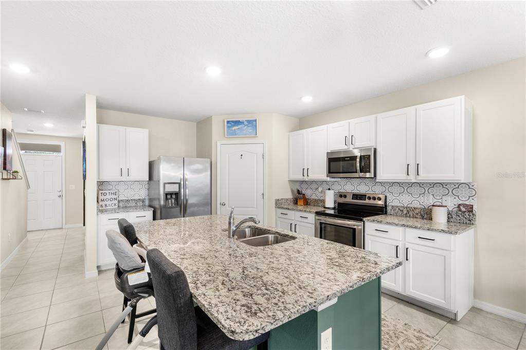 A kitchen features white cabinets, granite countertops, a central island, and stainless steel appliances — 9024 ALBA LANE, KISSIMMEE, FL