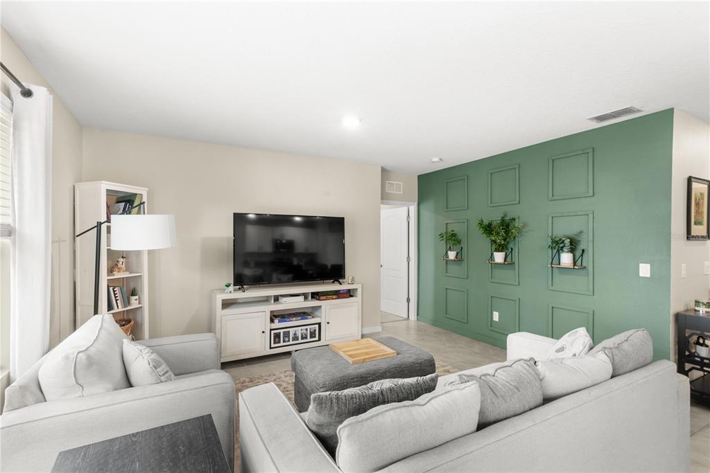 A living room features a green accent wall with molding and a white media console — 9024 ALBA LANE, KISSIMMEE, FL