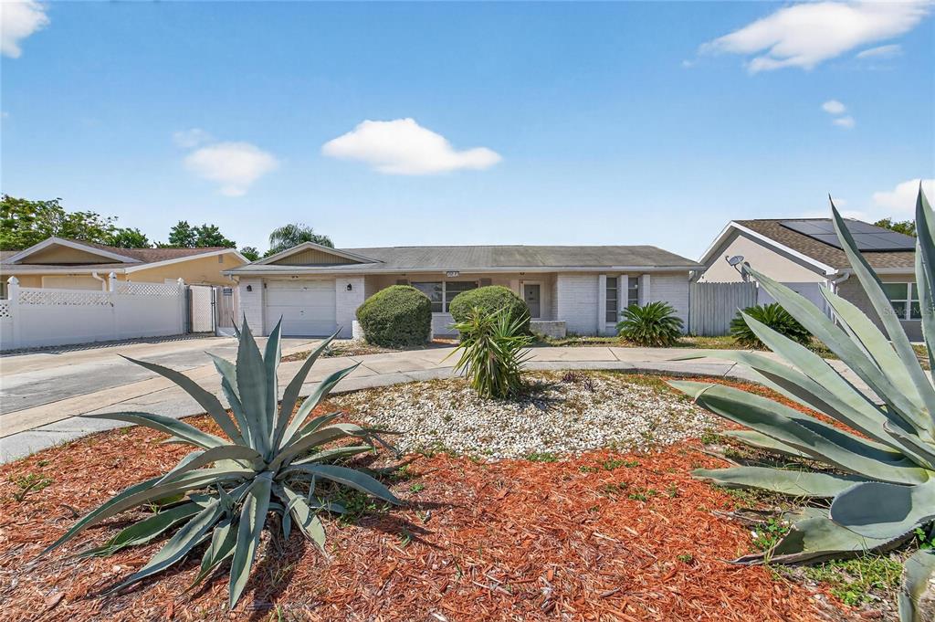A single-story house with a white brick facade, a garage, and a landscaped front yard — 10841 PICCADILLY ROAD, PORT RICHEY, FL