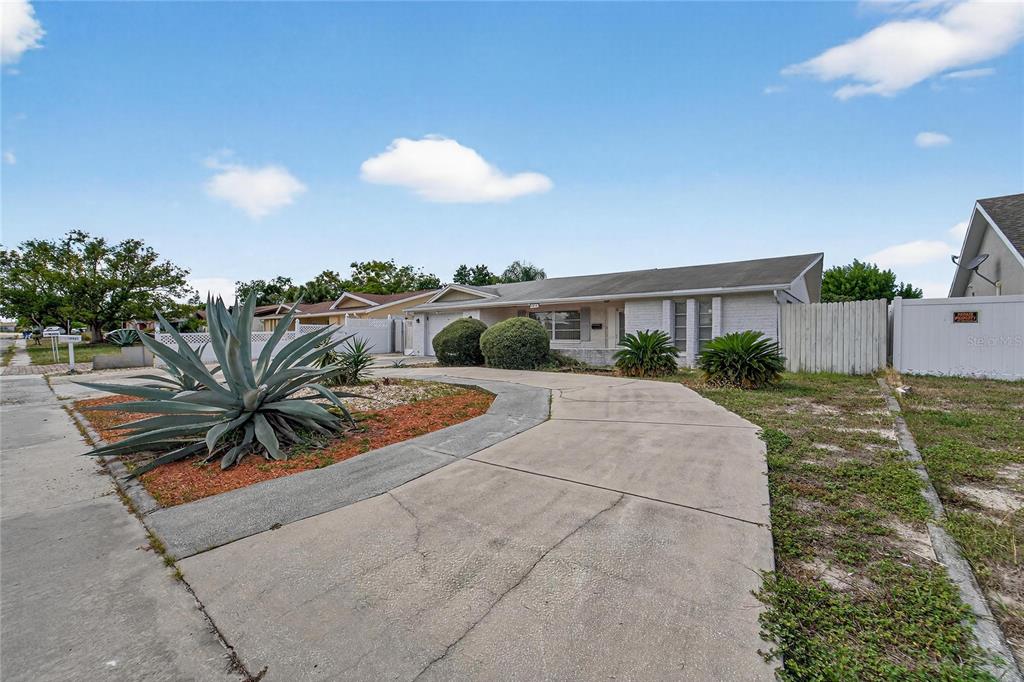 A single-story house with a concrete driveway, a large agave plant, and a white fence — 10841 PICCADILLY ROAD, PORT RICHEY, FL