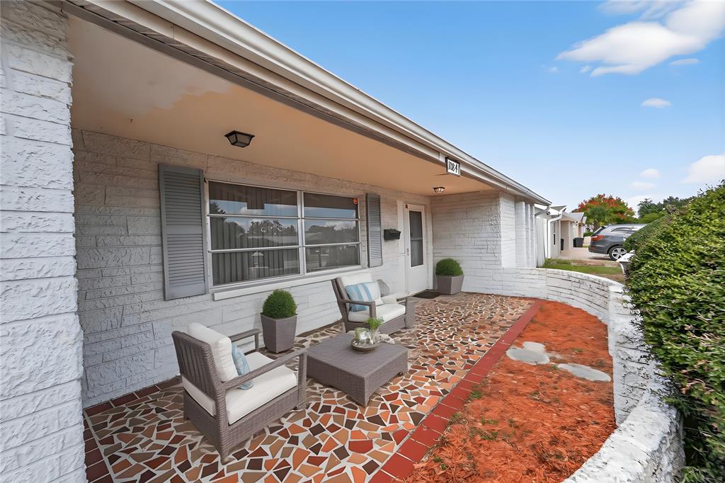 A covered patio features a mosaic tile floor, wicker furniture, and a low stone wall — 10841 PICCADILLY ROAD, PORT RICHEY, FL
