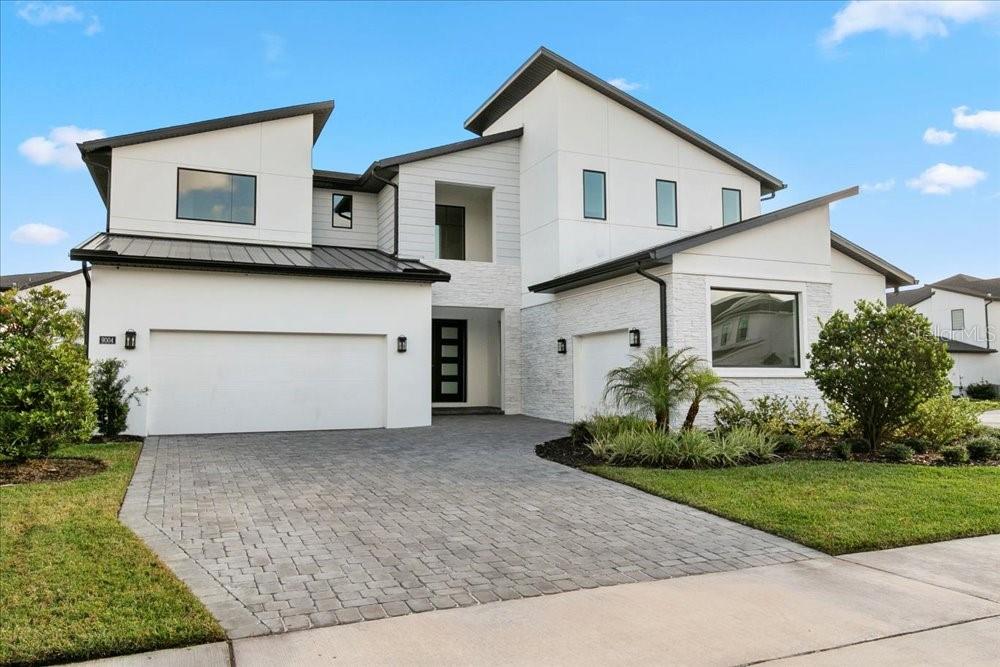 A modern two-story house features a white exterior, stone accents, and a paved driveway — 9004 SANTORINI DRIVE, ORLANDO, FL