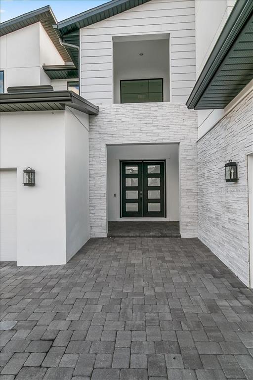 A modern home exterior features a stone-clad entryway, dark double doors, and paved driveway — 9004 SANTORINI DRIVE, ORLANDO, FL