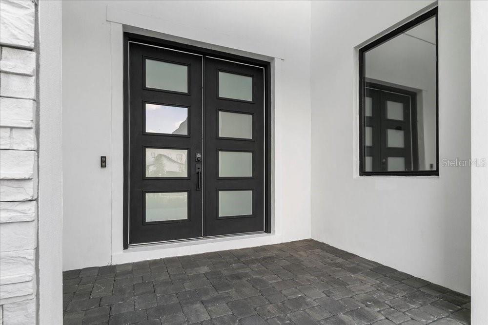A modern double front door with four glass panels opens onto a paved entryway — 9004 SANTORINI DRIVE, ORLANDO, FL