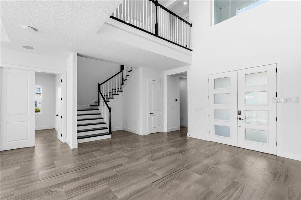 A bright foyer features a staircase with black railings, white double doors, and tiled flooring — 9004 SANTORINI DRIVE, ORLANDO, FL
