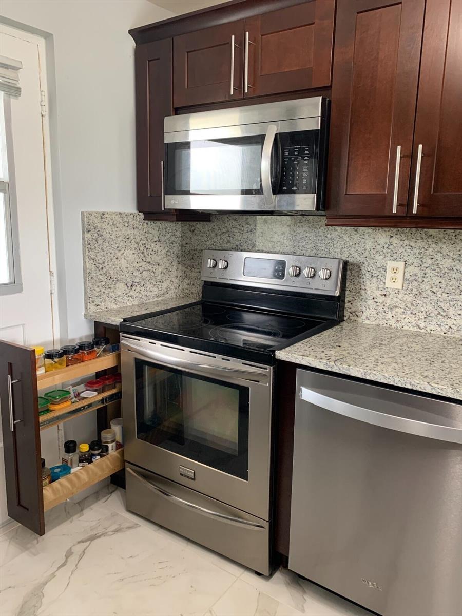 A kitchen features dark wood cabinets, granite countertops, stainless steel appliances, and a glass door — 5700 NW 2nd Avenue # 311, Boca Raton FL 33487, BOCA RATON, FL