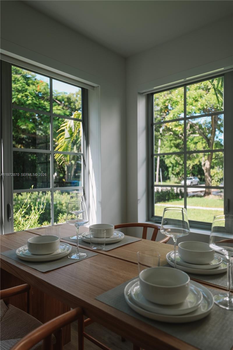 A dining area features a wooden table set for four with large windows overlooking trees — 128 NE 46th St # 3, Miami FL 33137, MIAMI, FL
