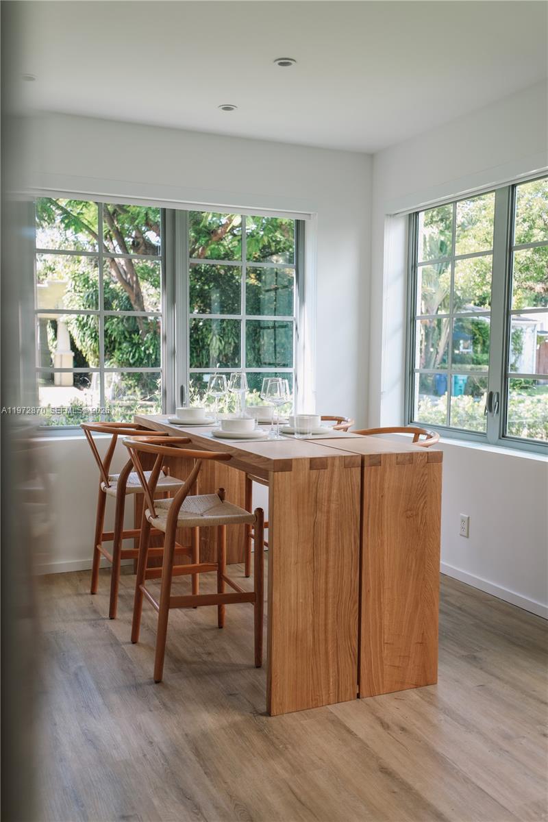 A dining area features a wooden table with four chairs set before large windows — 128 NE 46th St # 3, Miami FL 33137, MIAMI, FL